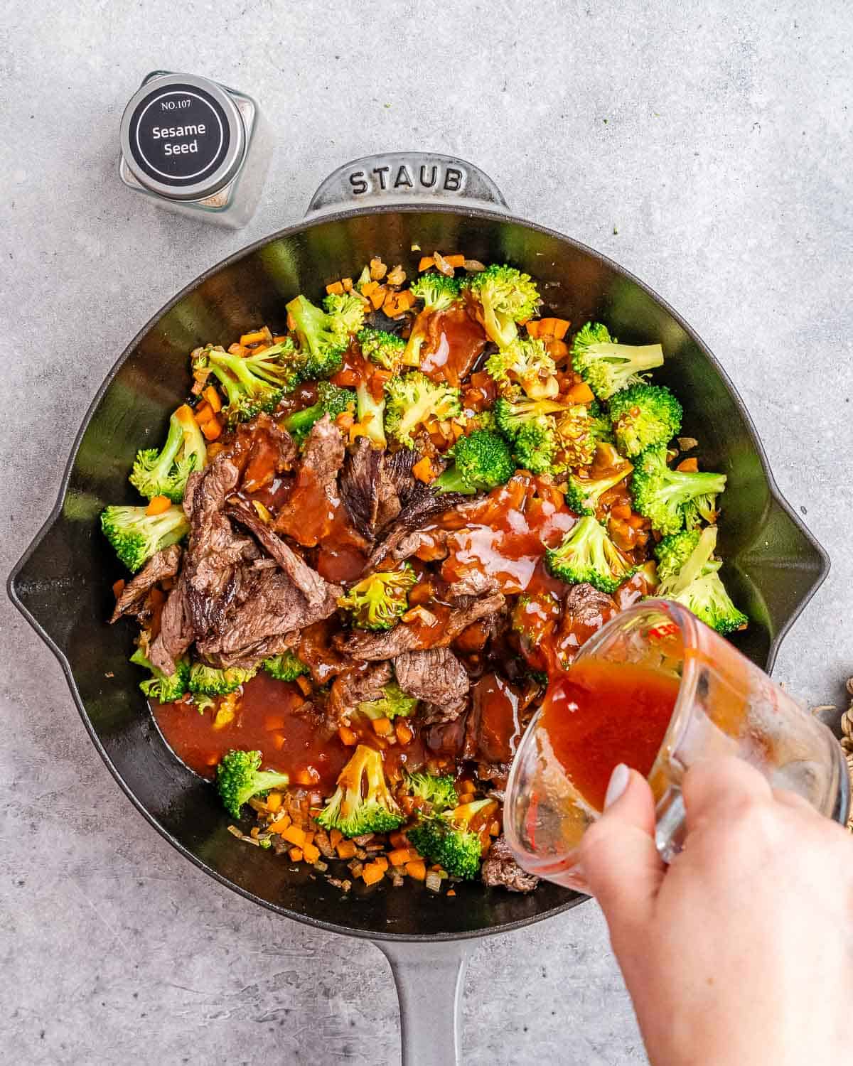 Pouring sauce over a skillet with vegetables and beef.