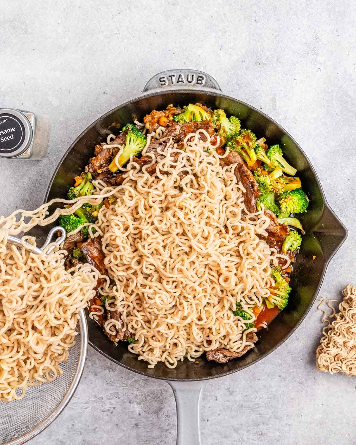 Pouring noodles into a skillet with broccoli and beef.