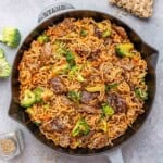 A black and gray skillet with noodles and seared beef and broccoli.