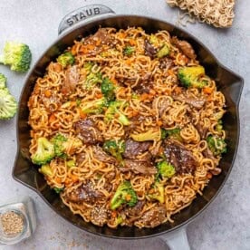 A black and gray skillet with noodles and seared beef and broccoli.