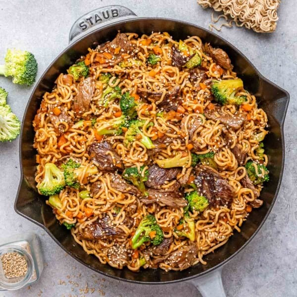A black and gray skillet with noodles and seared beef and broccoli.