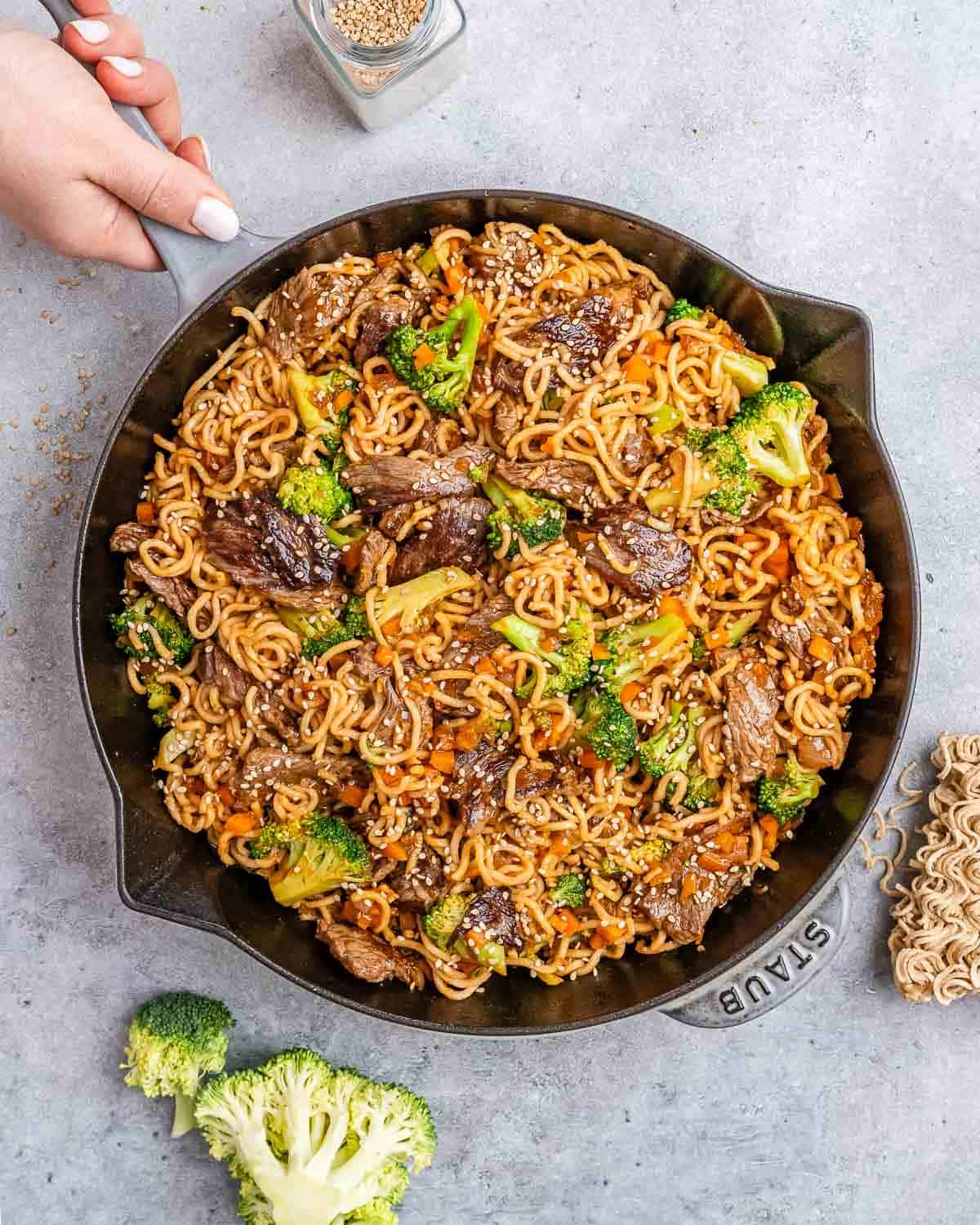 Beef lo mein in a cast iron skillet on a gray background.