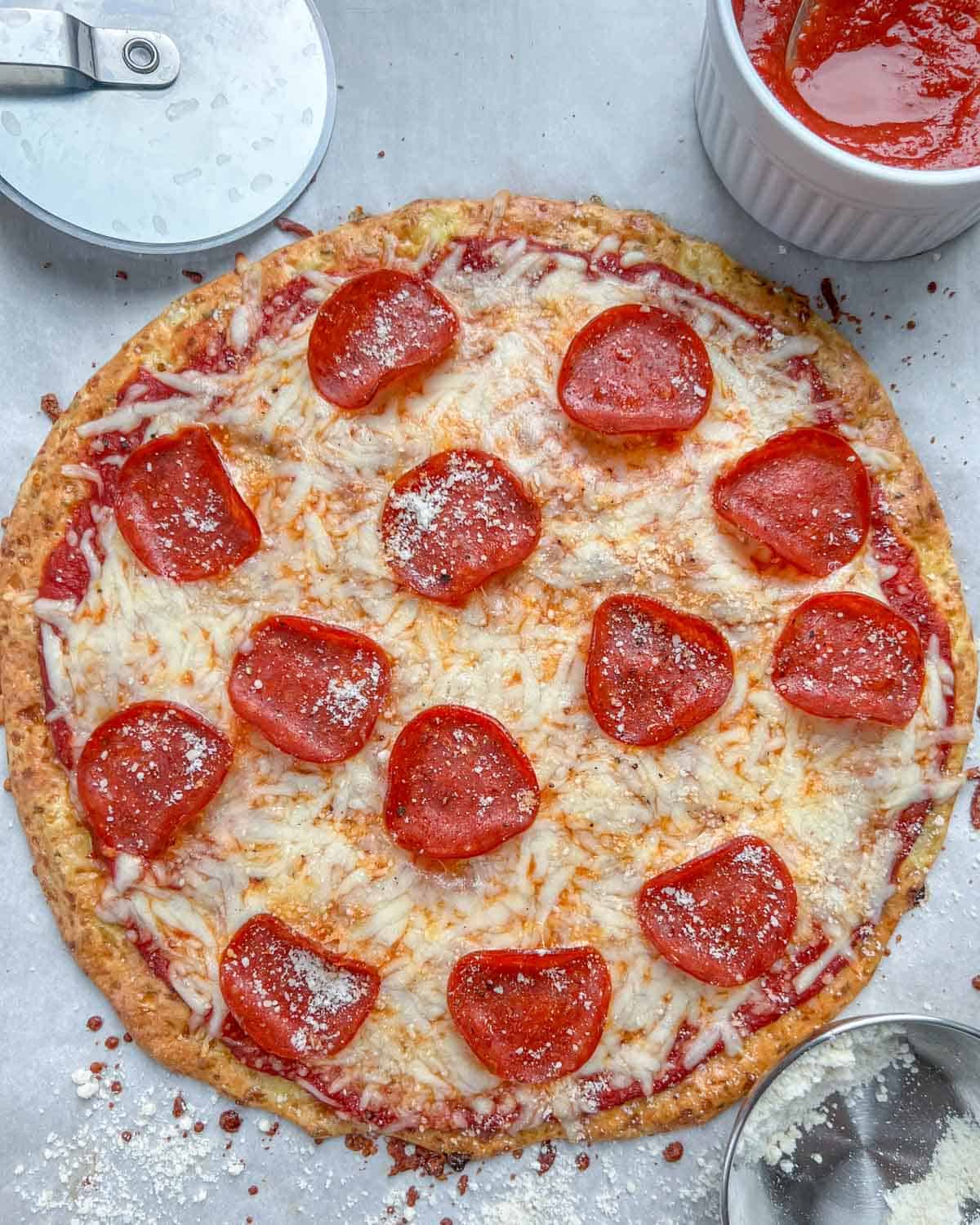 Round pizza topped with pepperoni with a small bowl or pizza sauce.