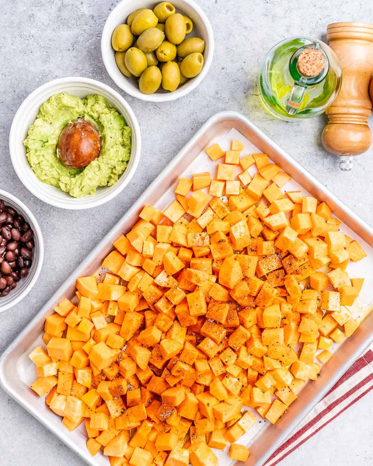 Diced sweet potatoes tossed with olive oil and seasoning, ready to be roasted, on a sheet pan next to other taco ingredients.