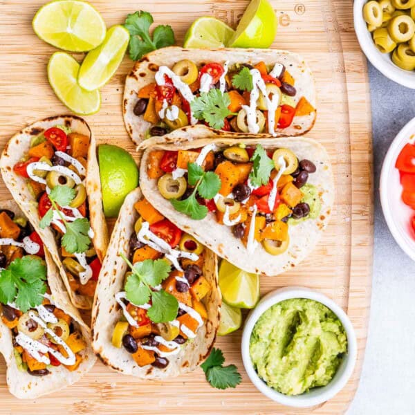 4 tacos filled with black beans and sweet potatoes on a cutting board.