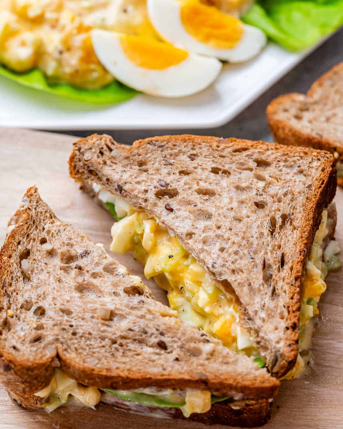 An egg salad sandwich cut in a triangle on a cutting board.