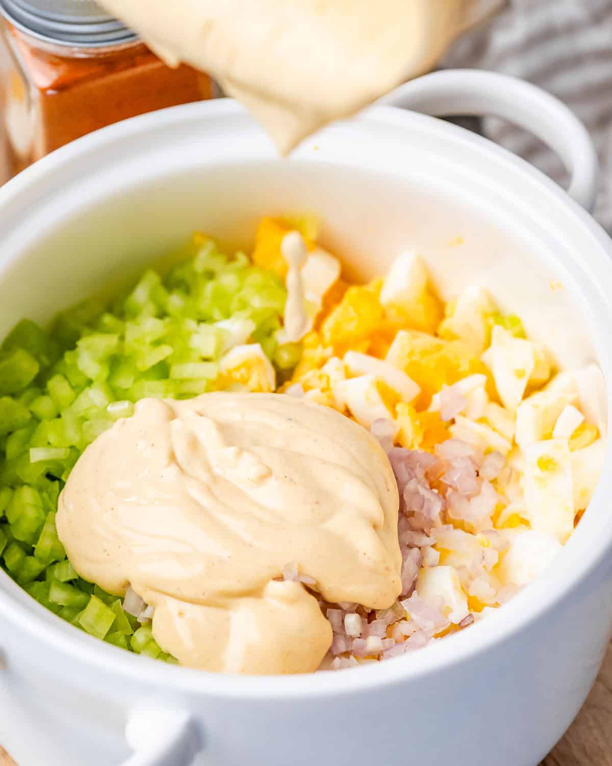 Pouring mayonnaise over chopped ingredients in a white bowl.