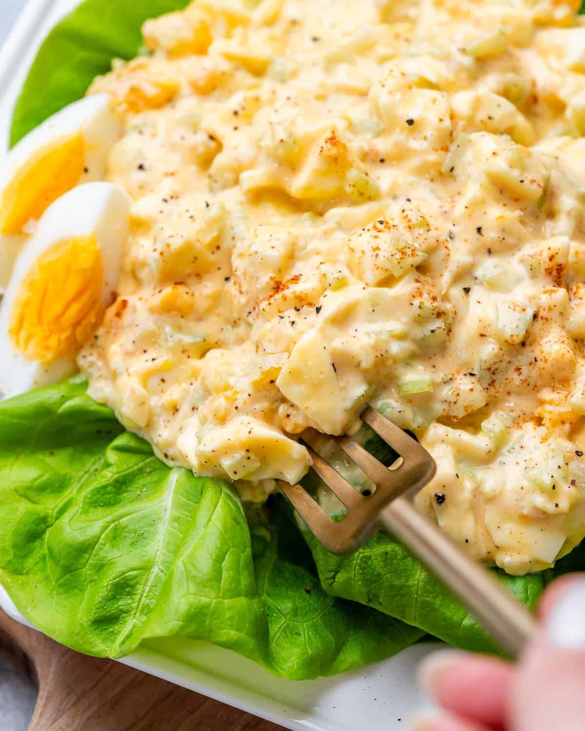 Egg salad being picked up by a fork on top of a lettuce leaf.