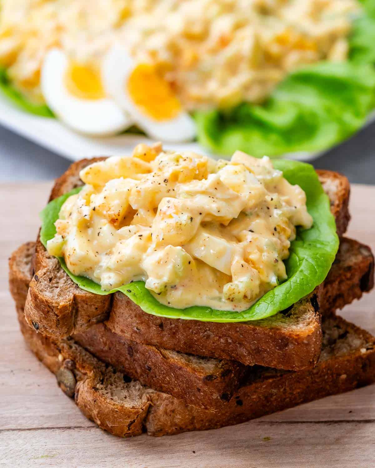 3 toast stacked on each other on a cutting board topped with egg salad over lettuce.