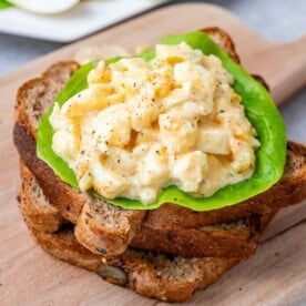 3 toast stacked on each other on a cutting board topped with egg salad over lettuce.