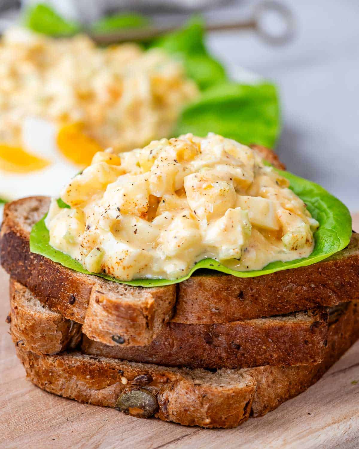 3 toast stacked on each other on a cutting board topped with egg salad over lettuce.