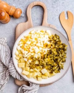 Potatoes, eggs, and pickles in a white bowl.