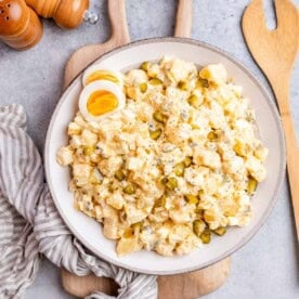 A large white plate with potato salad and a wooden spoon on the side.