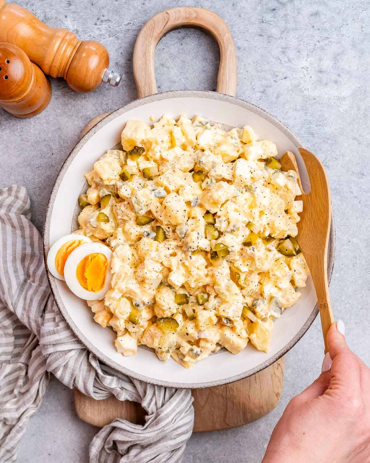 A large white plate with potato salad and a wooden spoon on the side. 