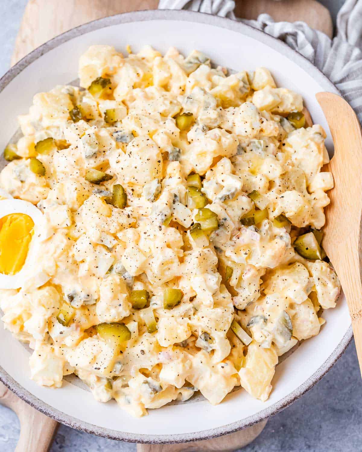 A large white plate with potato salad and a wooden spoon on the side.