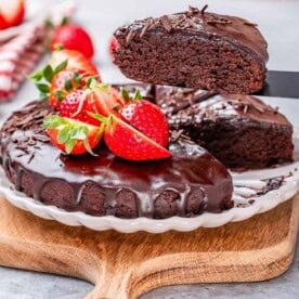 Chocolate cake on a plate top with melted chocolate and strawberries.