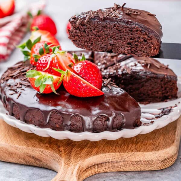 Chocolate cake on a plate top with melted chocolate and strawberries.