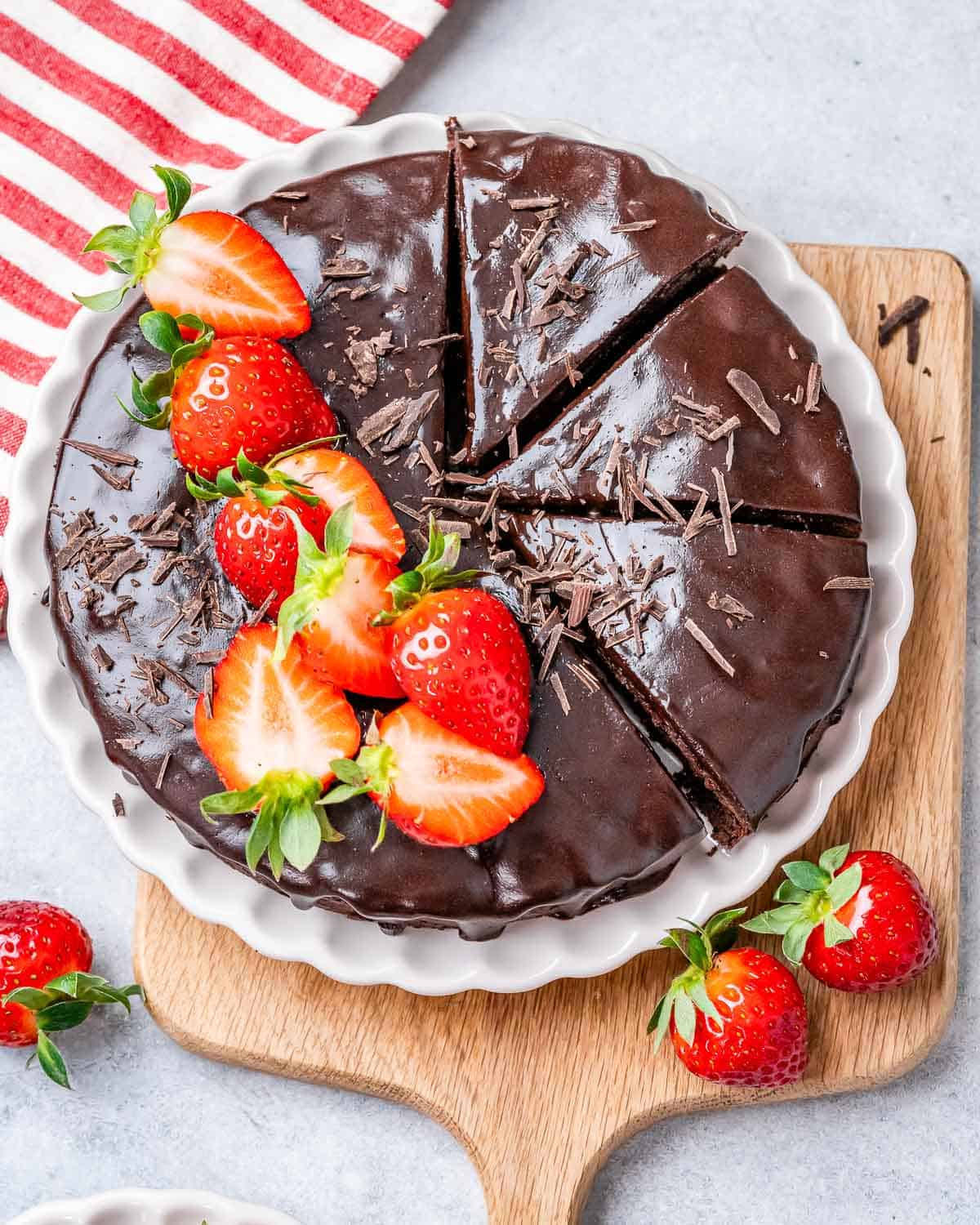 Chocolate cake on a plate top with melted chocolate and strawberries.