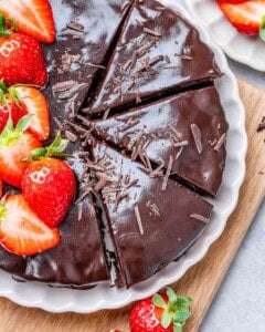 Chocolate cake on a plate top with melted chocolate and strawberries.