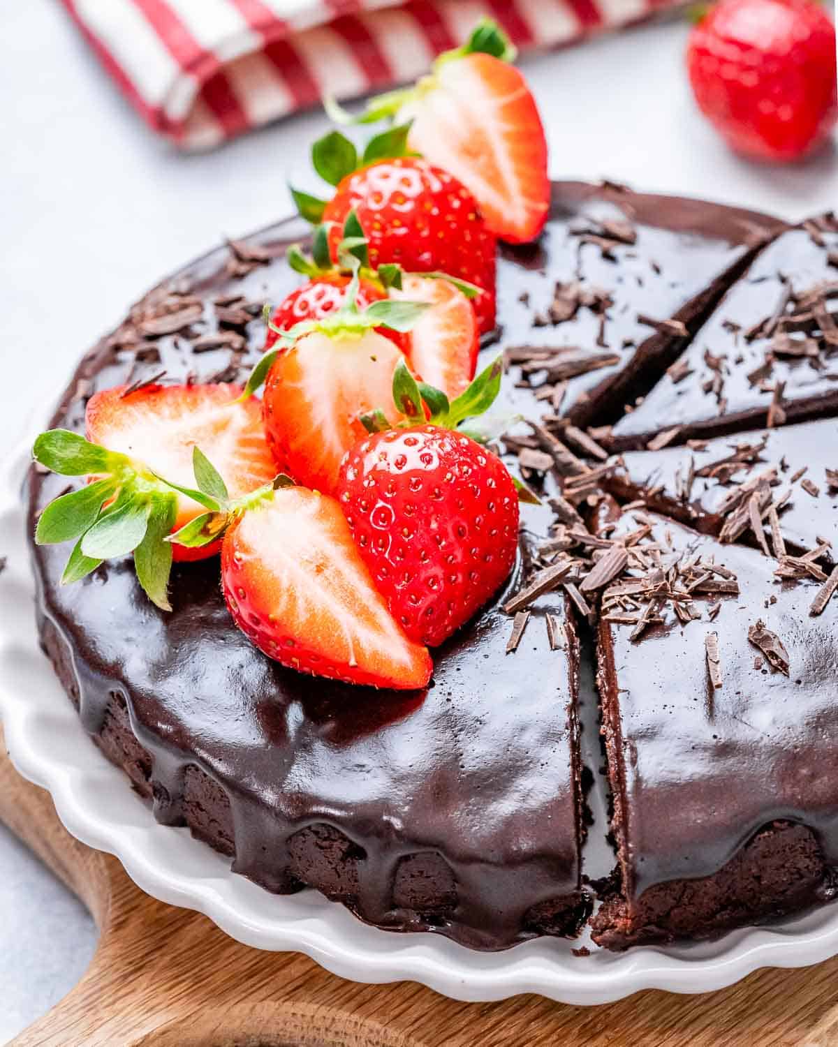 Chocolate cake on a plate top with melted chocolate and strawberries.