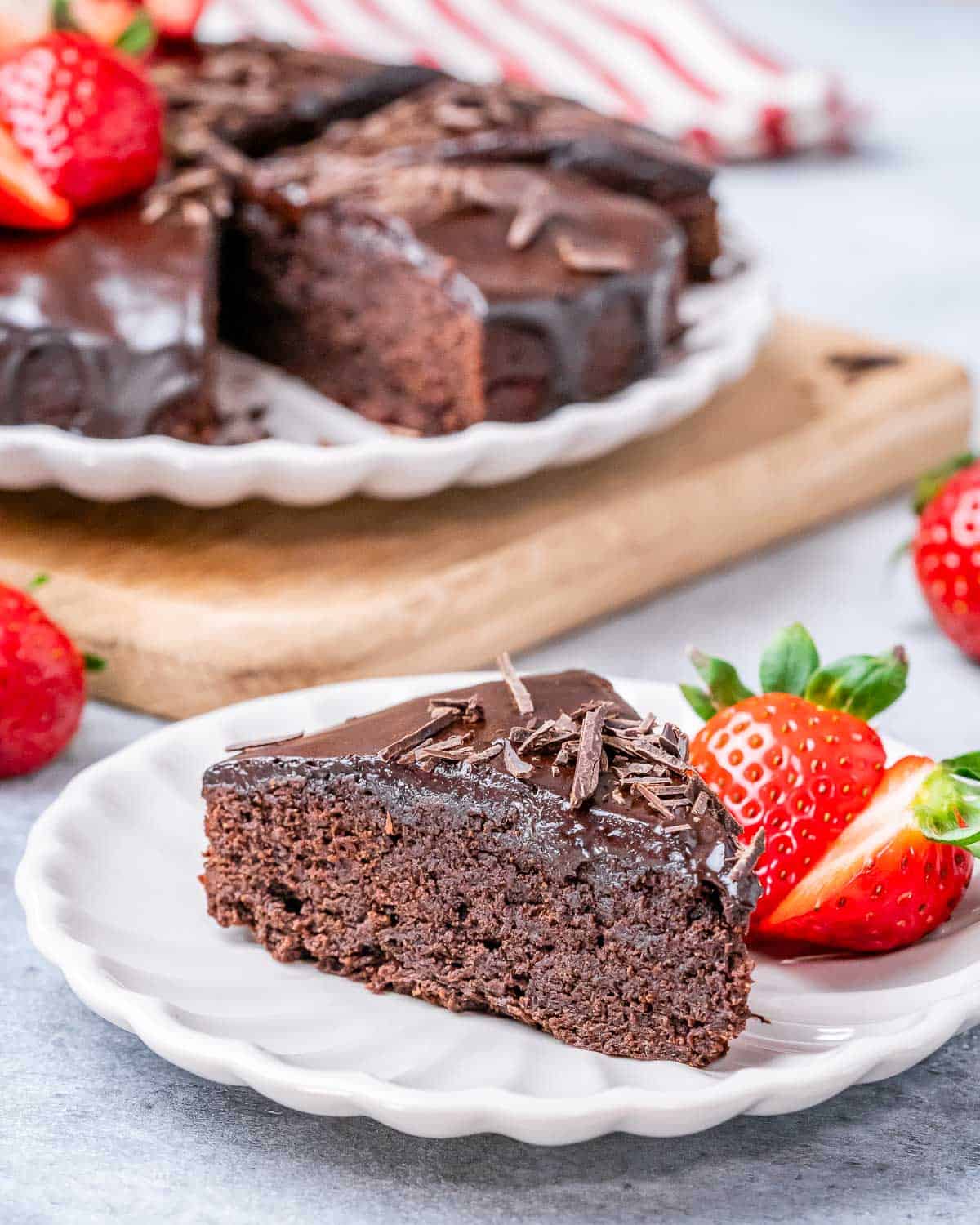 A slice of chocolate cake on a white plate with strawberries on the side.