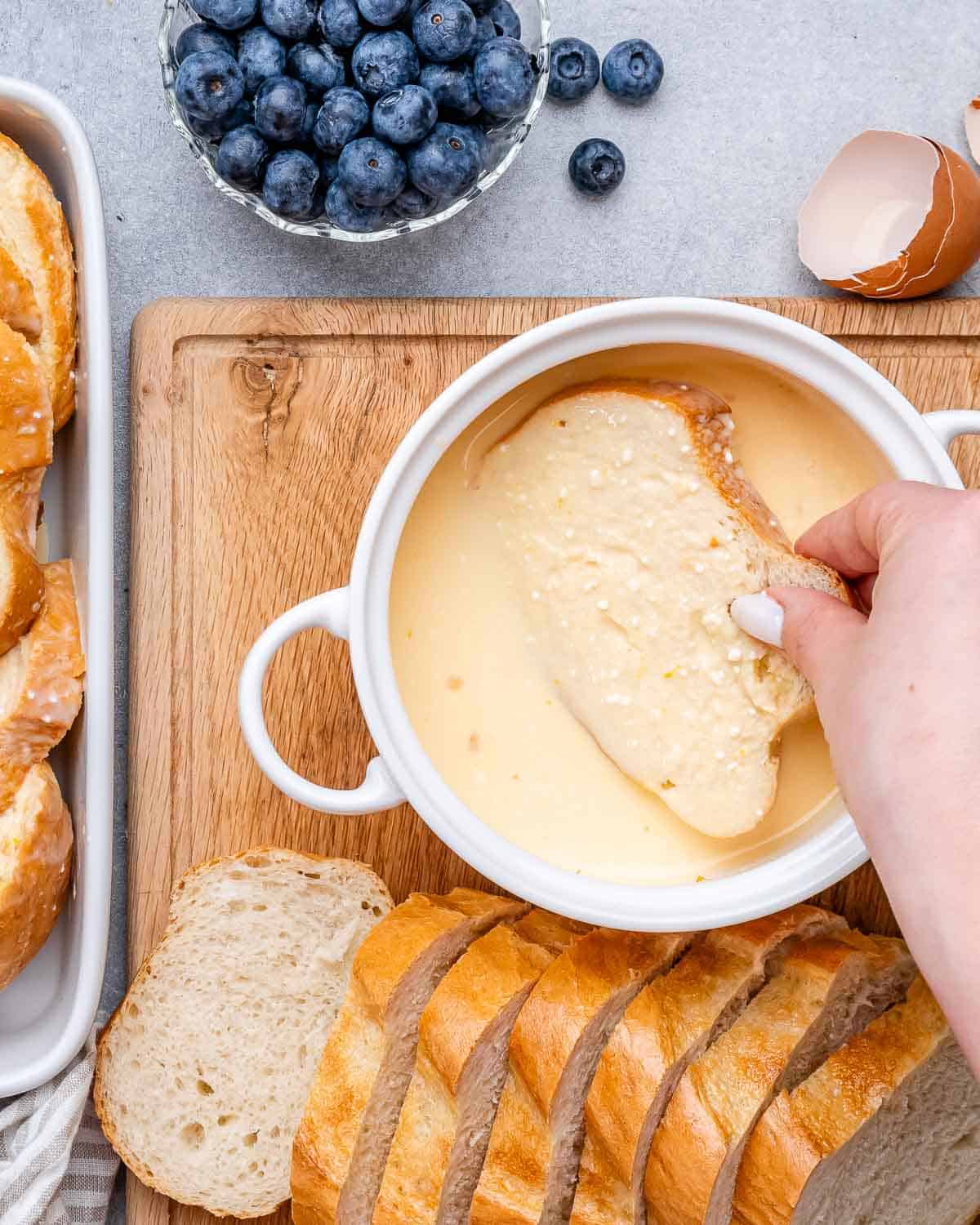 A hand dipping a slice of bread into an egg mixture.