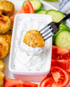 A fork dipping a meatball into white sauce.