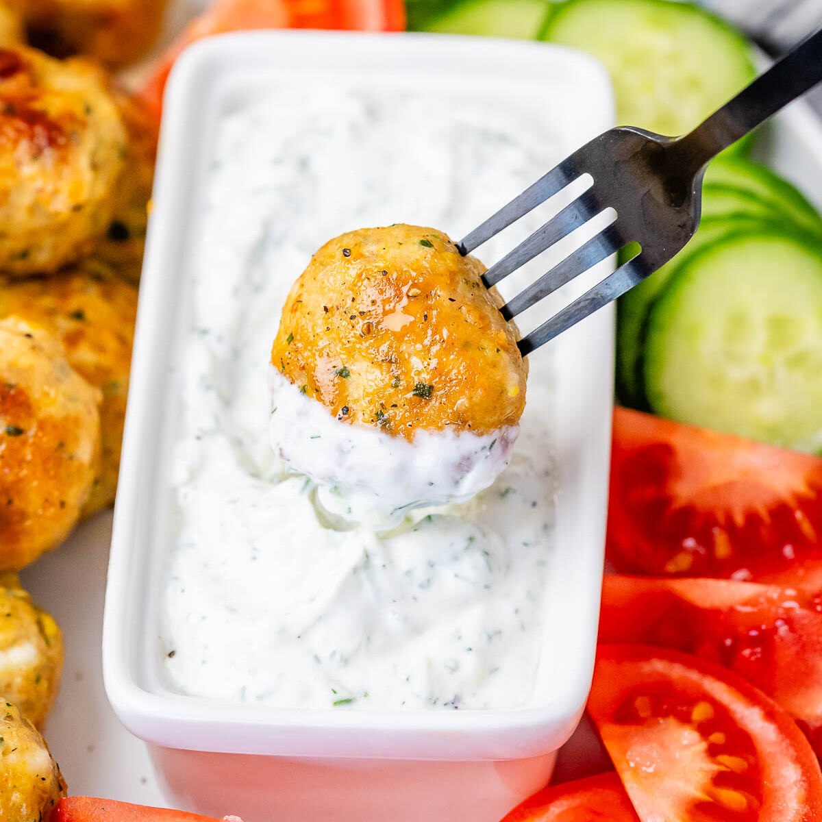 A fork dipping a meatball into white sauce.