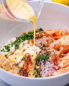 A measuring cup pouring sauce over a white bowl of ingredients.