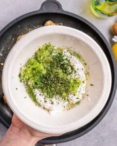 A hand holding a bowl with green herbs.