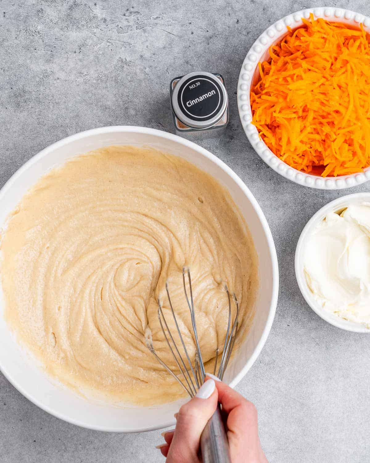 A whisk stirring cake batter in a white bowl.