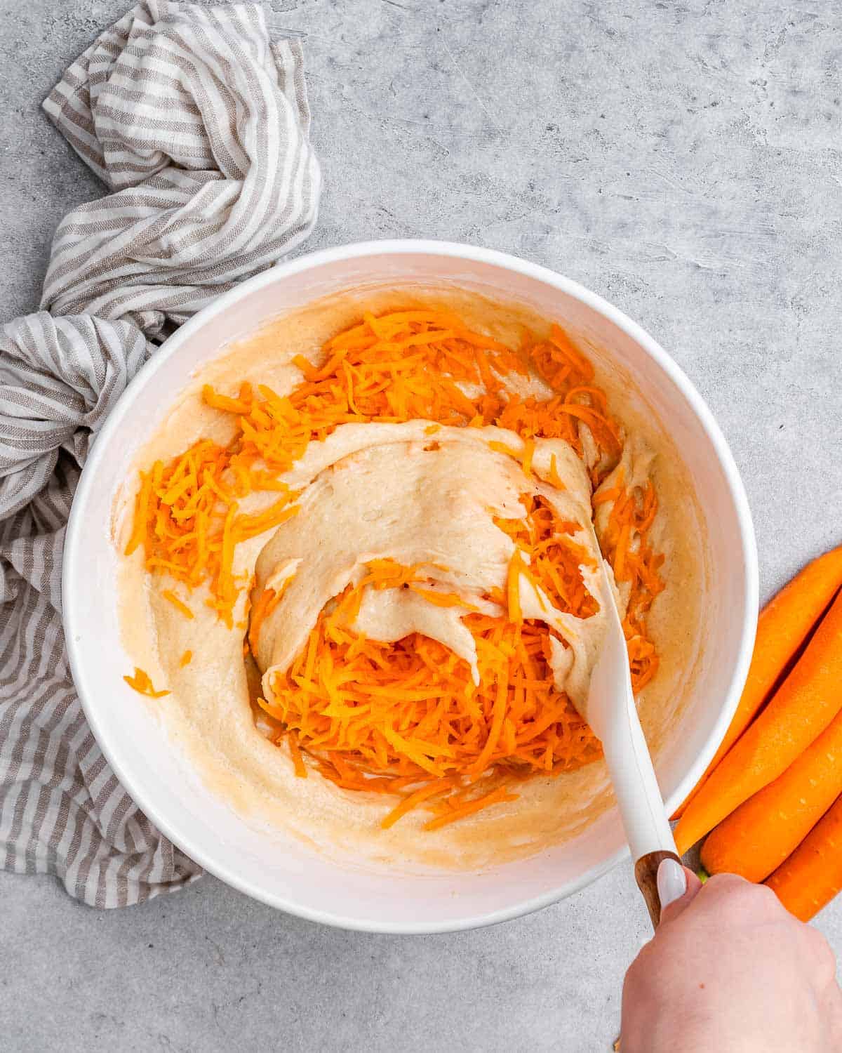 A spatula stirring in carrots to cake batter.