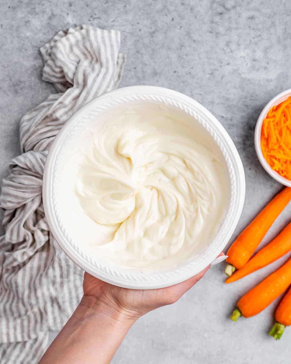 A hand holding whipped frosting in a bowl.