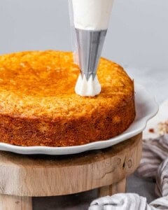 A frosting bag making a dot of frosting on an unfrosted orange cake.