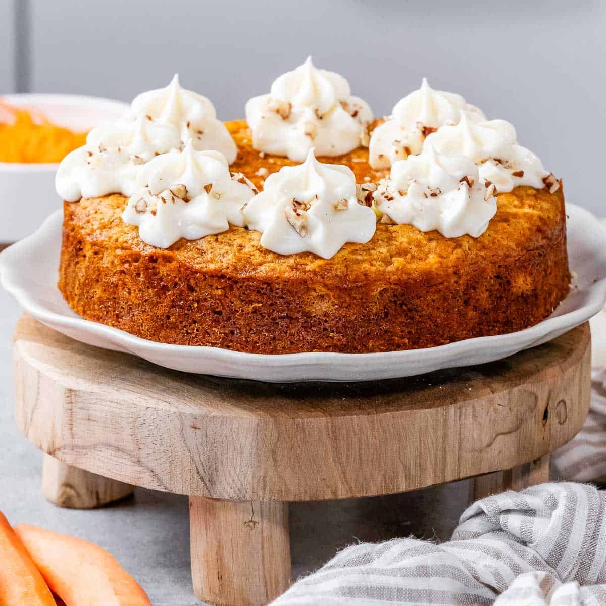 A round carrot cake with slice cut off topped with creamy cheese frosting.