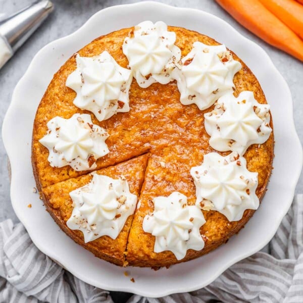 round carrot cake with slice cut off topped with creamy cheese frosting.