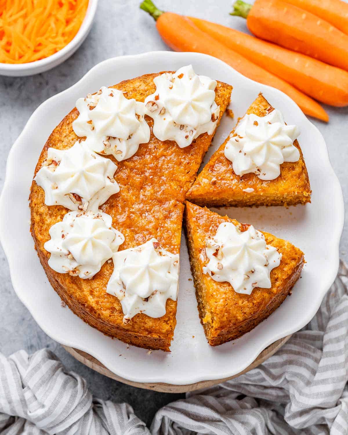 A round carrot cake with slice cut off topped with creamy cheese frosting.