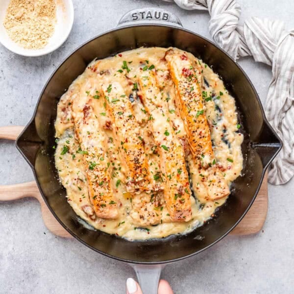 4 cooked salmon filets in a skillet over a creamy sauce.