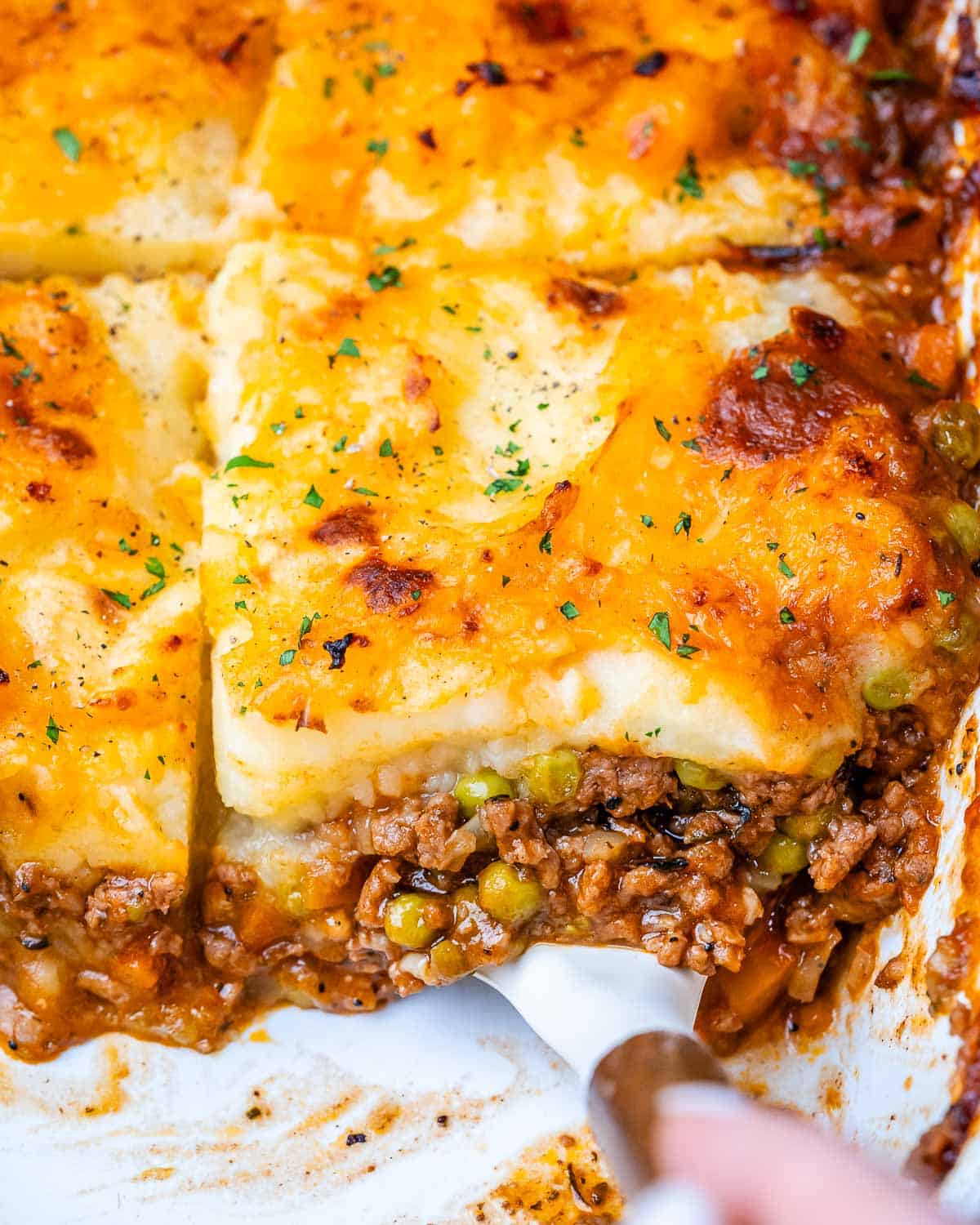 Shepherds pie in a white baking dish with meat showing at the bottom and potatoes on top.