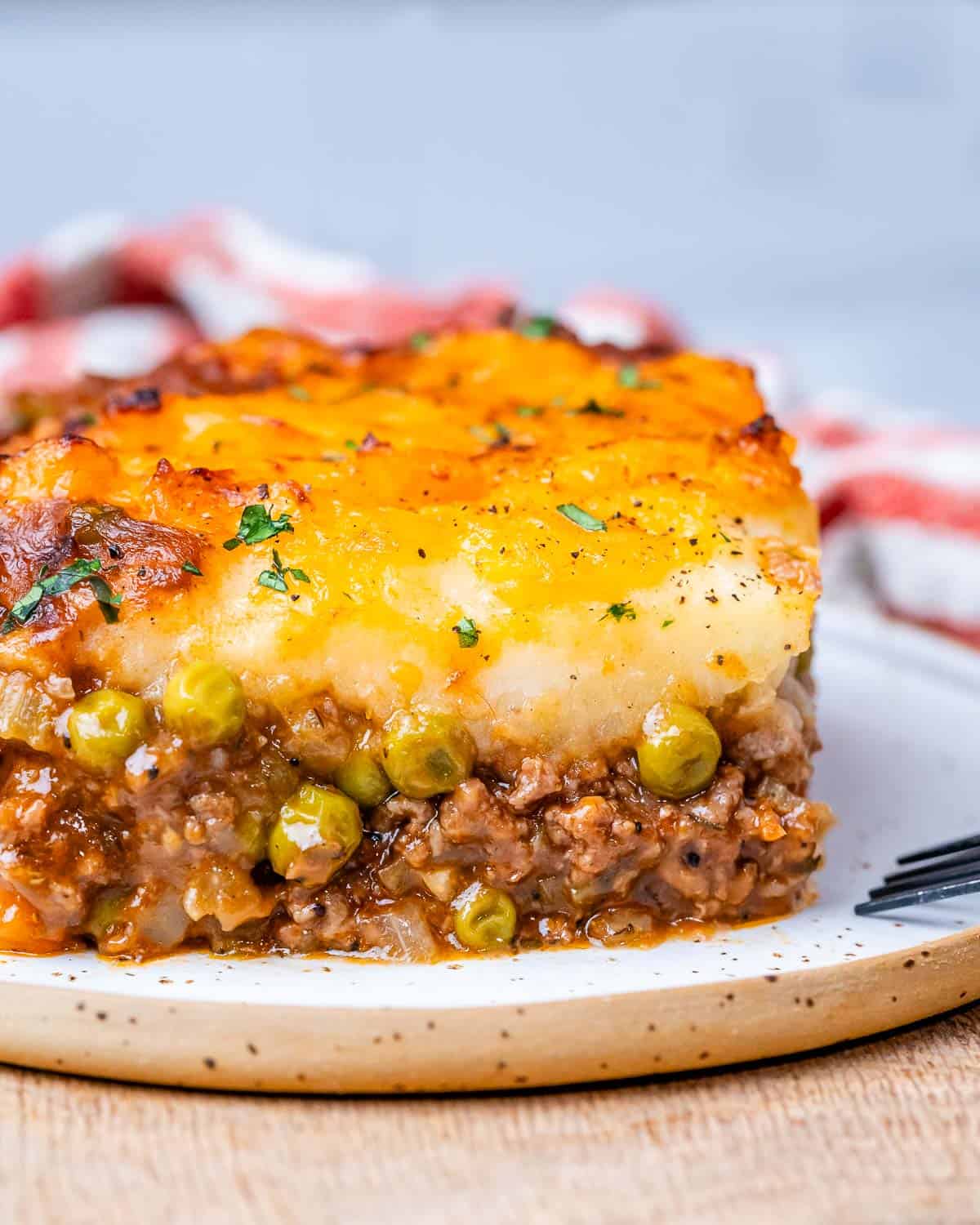 Shepherds pie on a white plate with meat showing at the bottom and potatoes on top.