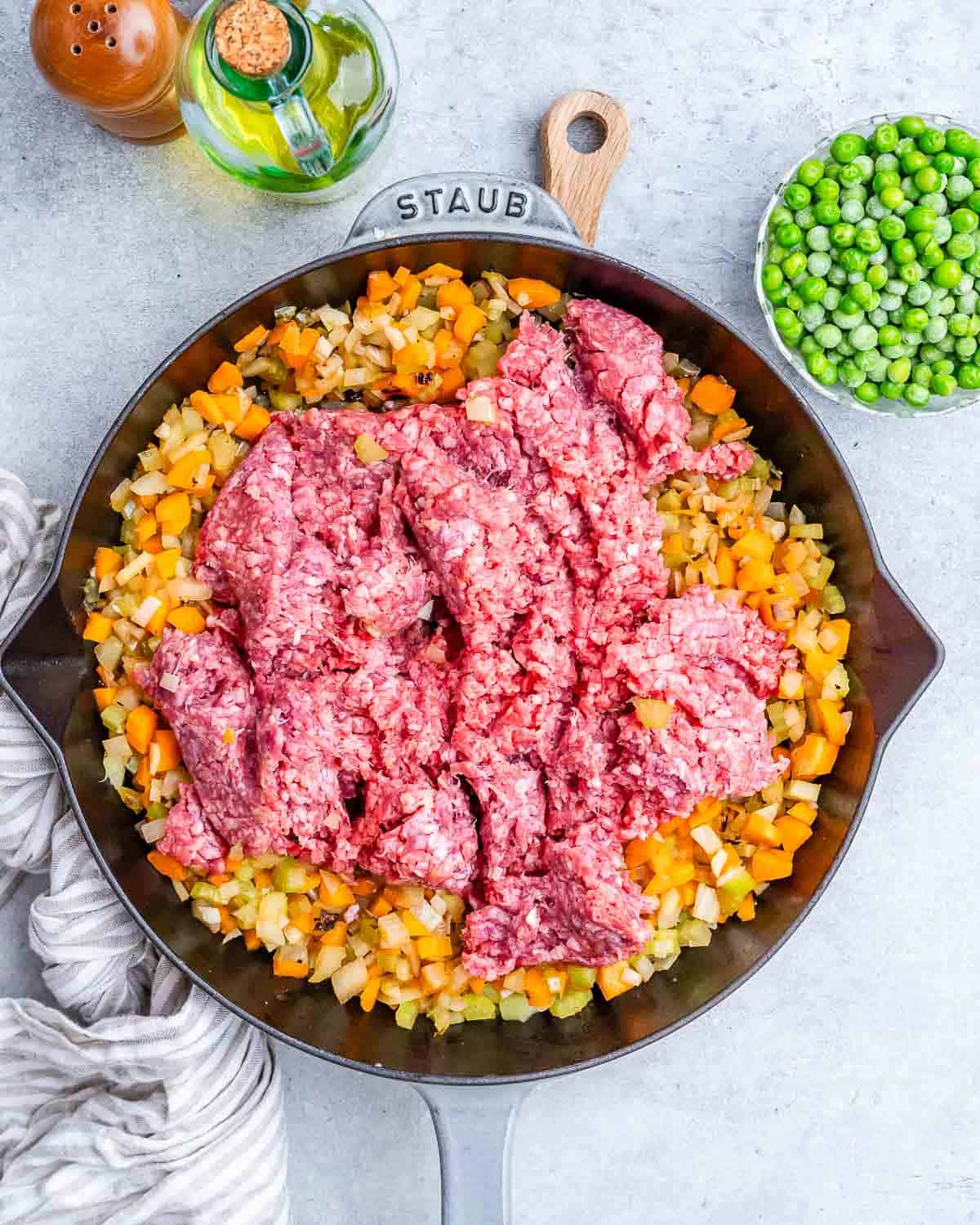 Raw ground beef over cooked veggies in a black skillet.