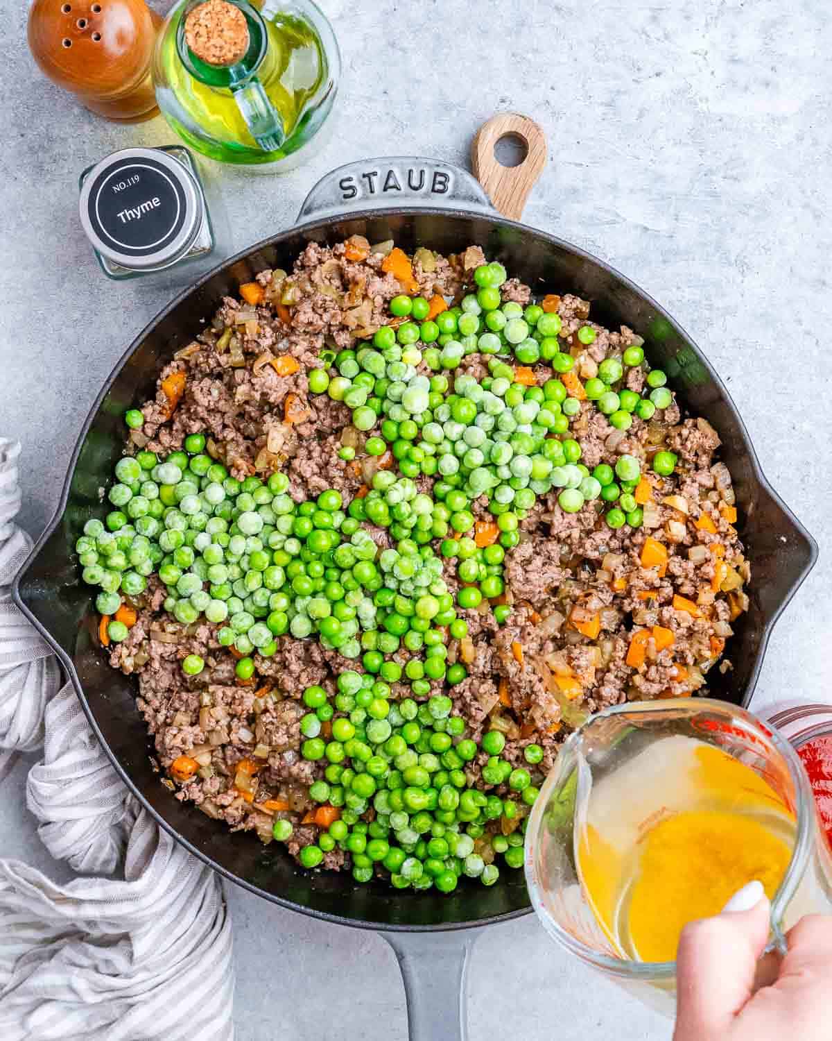 Pouring liquid from a measuring cup over beef and peas in a skillet.