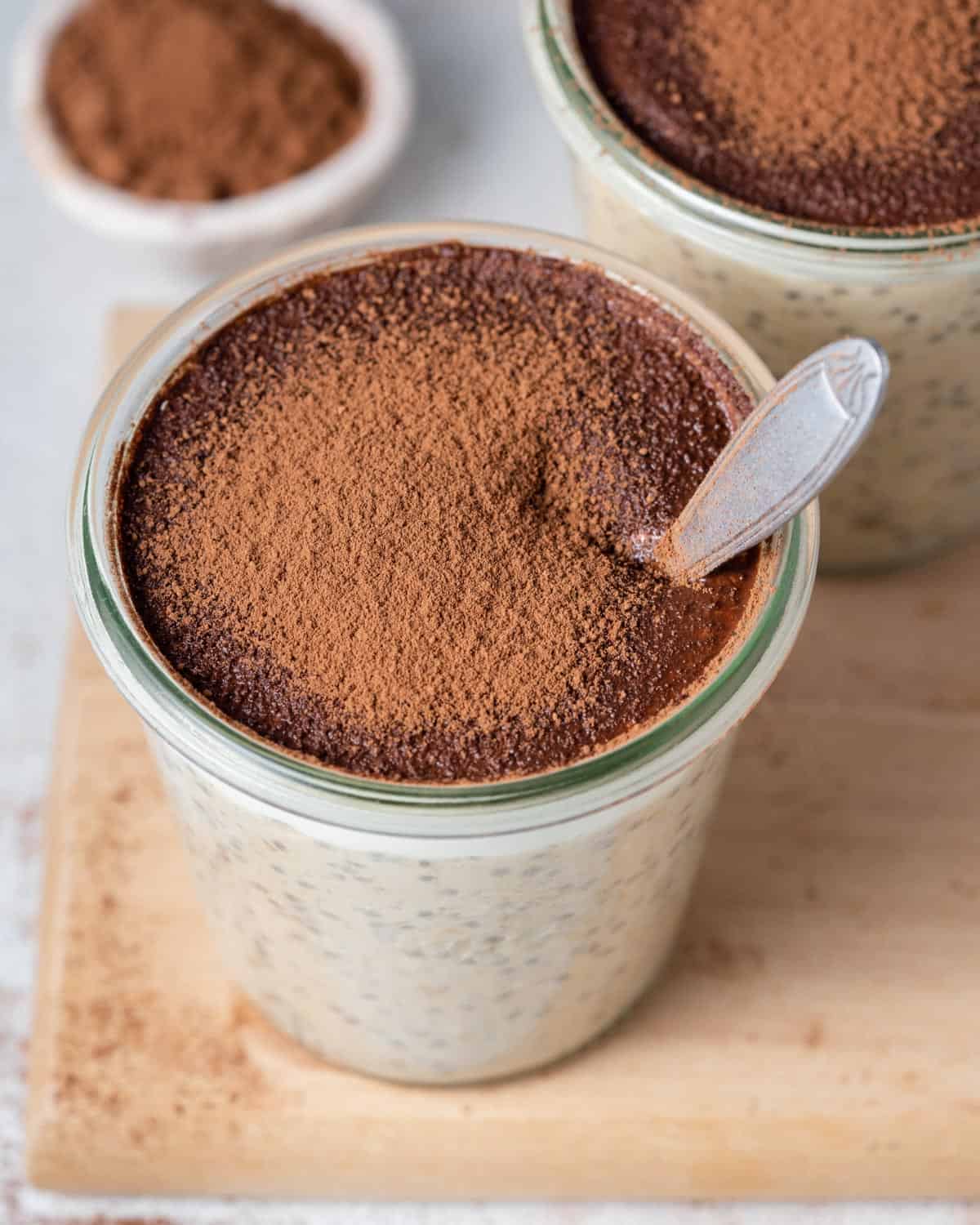 a spoon in a jar with white overnight oats topped with cocoa powder.