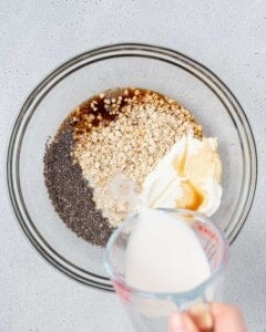 Milk being poured into a bowl with oats, chia, and yogurt.