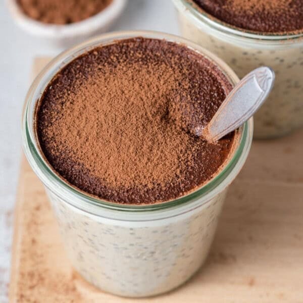 a jar with overnight oats topped with cocoa powder and a spoon in the jar.