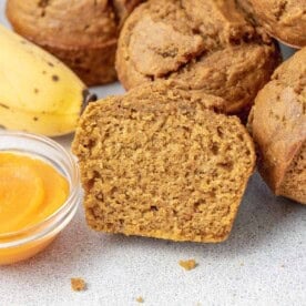 a sliced pumpkin muffin by a bowl of pumpkin sauce and other muffins.