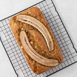 banana bread on a wire rack with two sliced bananas over the bread.