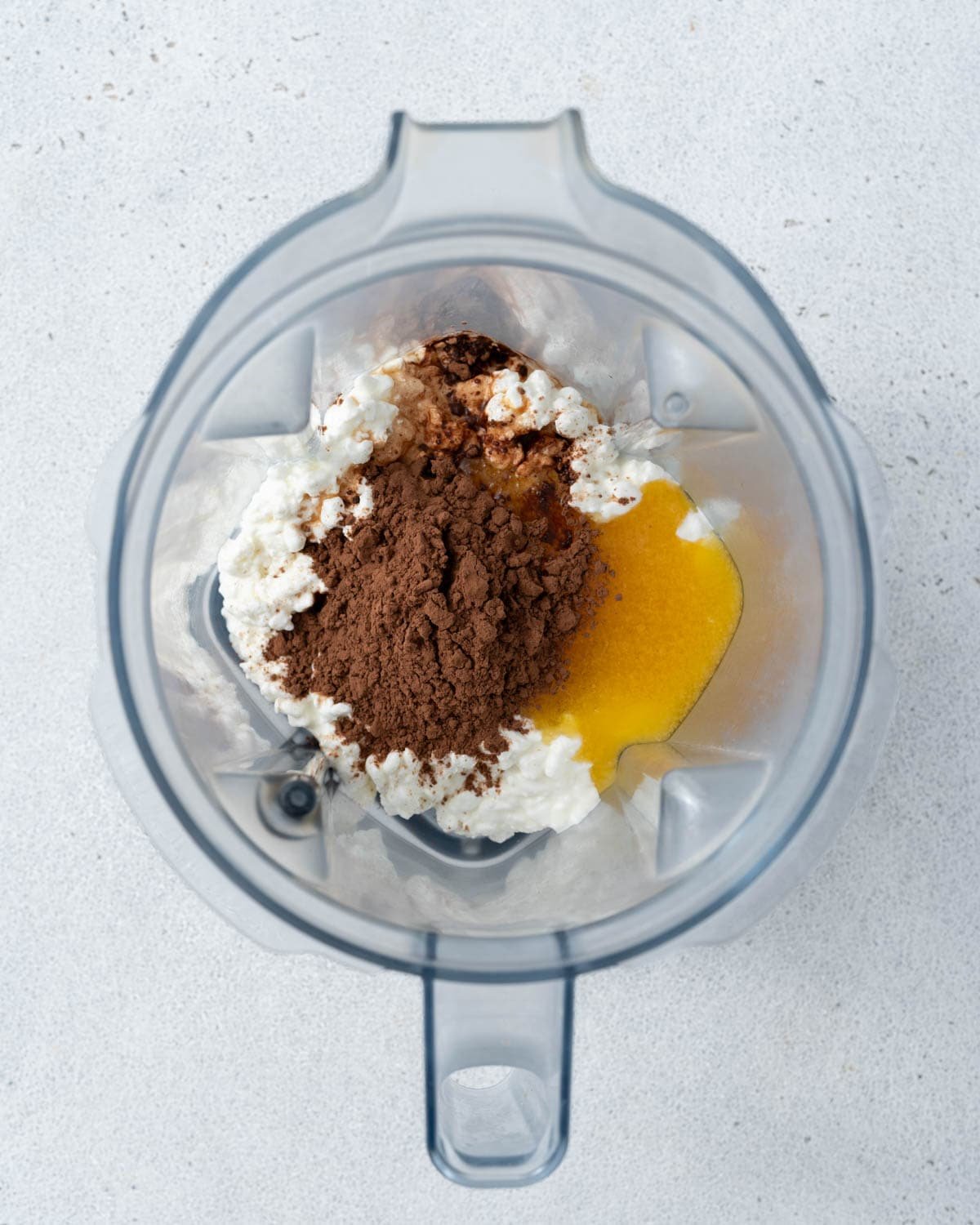 Ingredients inside a blender before mixing: cottage cheese, cocoa powder, and sweetener.