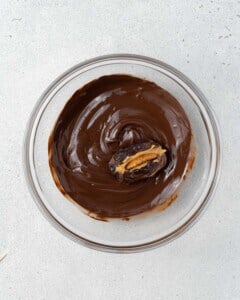A single date being dipped in the bowl of melted chocolate