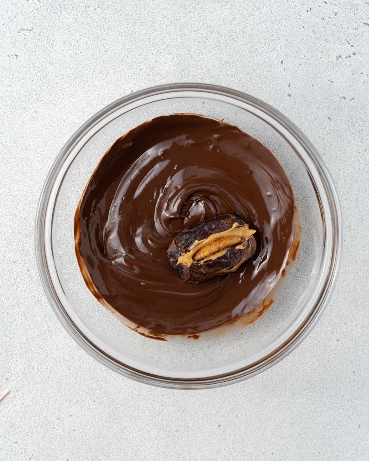 A single date being dipped in the bowl of melted chocolate